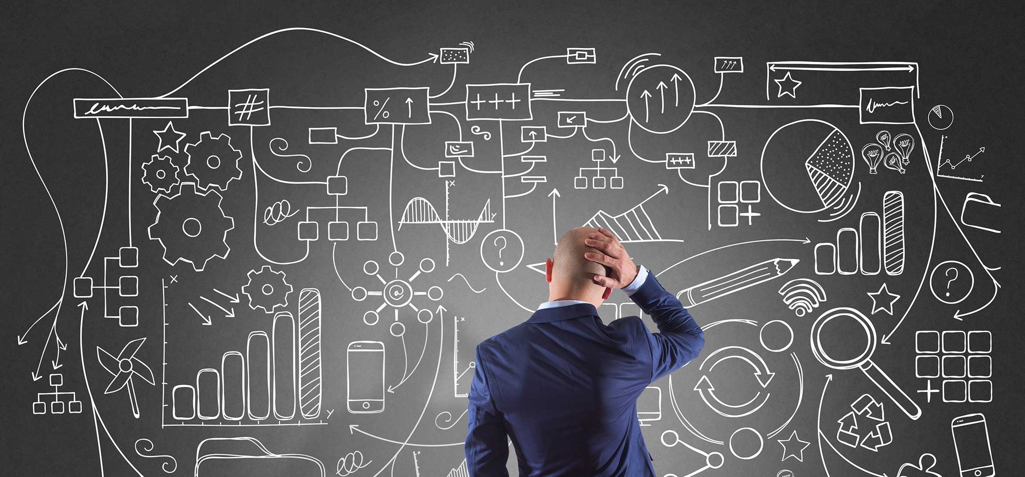 A man in a suit looks at a chalkboard filled with diagrams and graphs. 