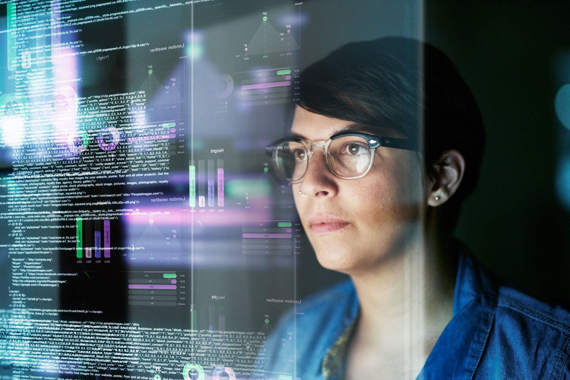 A serious woman with glasses looks at colorful data displayed on a screen.
